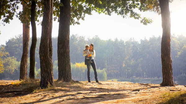 Cheerful smiling mother holding her 1 year old baby son in autumn park
