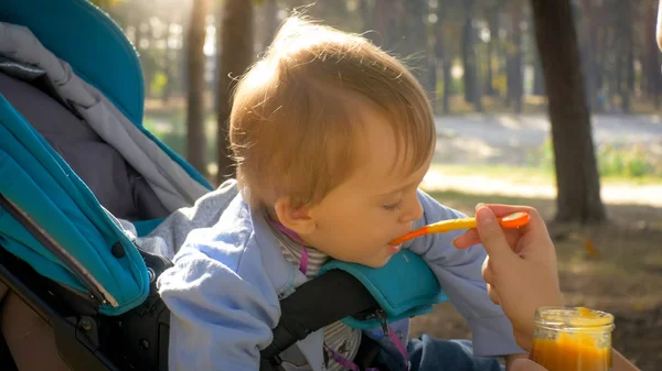 Closeup image of cute baby boy eating porridge from spoon at park — Stock Photo, Image