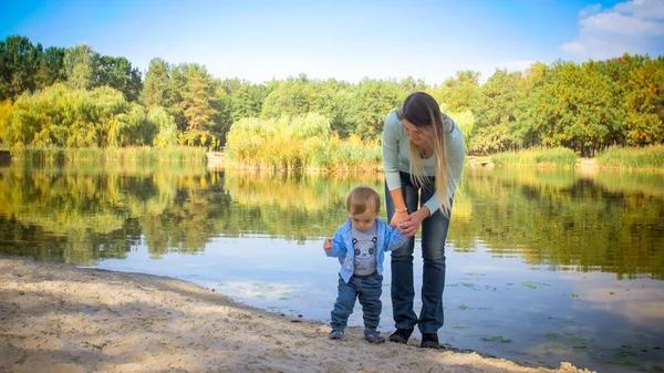 公園にある大きな湖で彼女の幼児の息子に立っている若い女性 — ストック写真