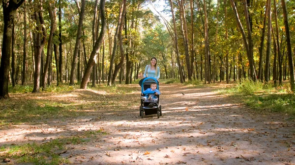 Szczęśliwy uśmiechający się kobieta spaceru w parku z dzieckiem w wózku — Zdjęcie stockowe