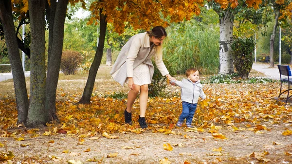 Ładny toddler chłopiec chodzenie z matki pod drzewem w parku jesień — Zdjęcie stockowe