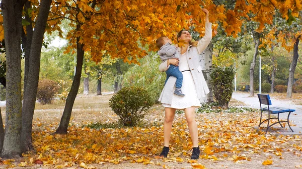 Menino criança feliz com a mãe olhando em folhas amarelas no parque de outono — Fotografia de Stock