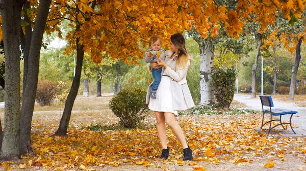 Hermosa madre sonriente dando hoja amarilla del árbol en el parque —  Fotos de Stock