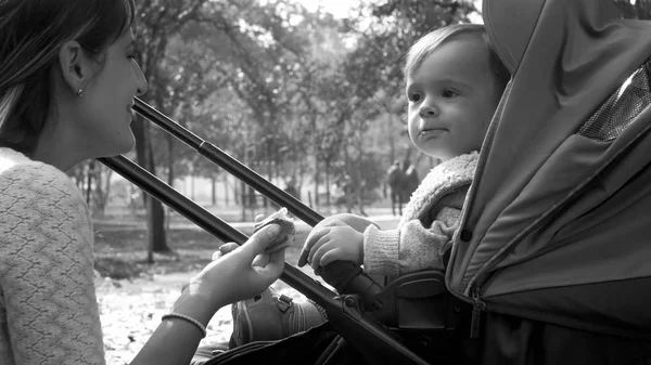 Zwart-wit portret van schattige peuter jongen eten in kinderwagen in het park — Stockfoto