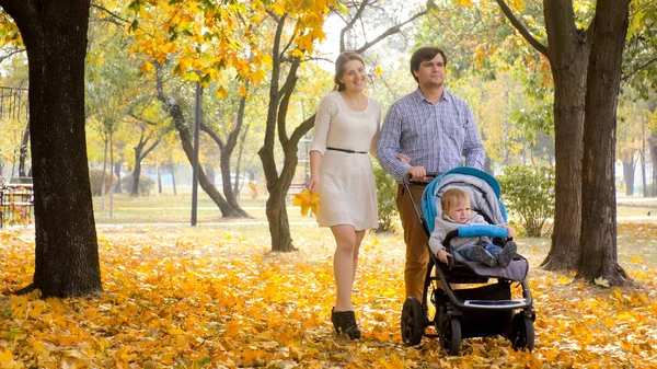 Улыбающаяся пара с маленьким мальчиком прогуливается по листьям в осеннем парке — стоковое фото