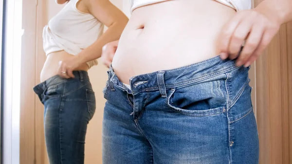 Closeup photo of young woman with big belly wearing tight jeans at mirror — Stock Photo, Image