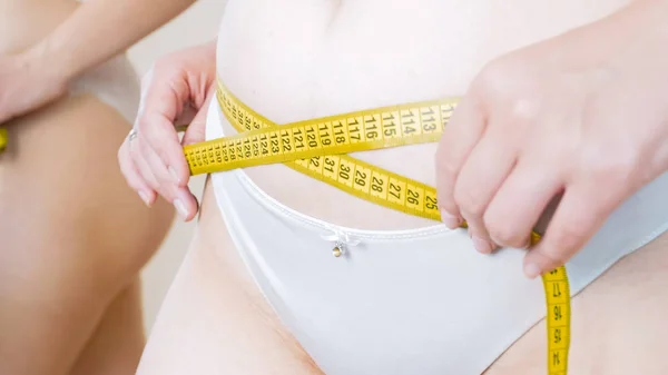 Mujer joven usando cinta métrica para medir su cintura en el espejo —  Fotos de Stock