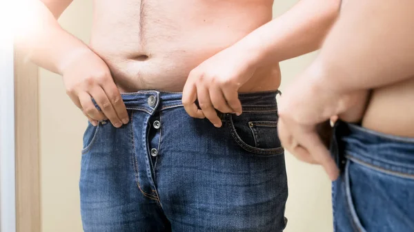 Closeup photo of young man fitting in small jeans at mirror — Stock Photo, Image