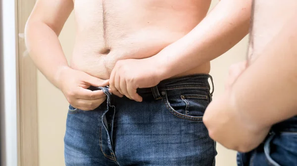 Young obese man struggling to button up tight jeans