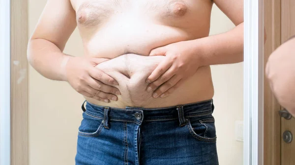 Detailní snímky tlustý muž v zrcadle drží své velké břicho — Stock fotografie