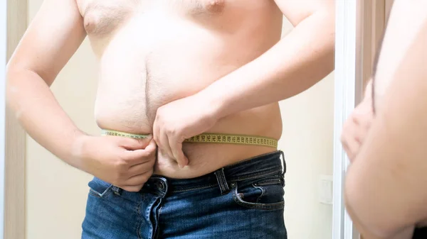 Genç şişko adam ayna onun büyük fat belly ölçmek için çalışıyorum — Stok fotoğraf