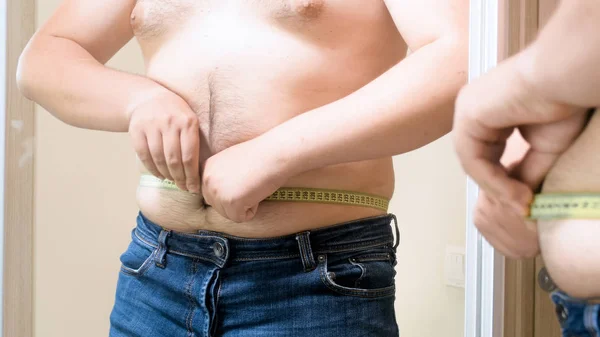 Young overweight man measuring his fat belly with measuring tape — Stock Photo, Image