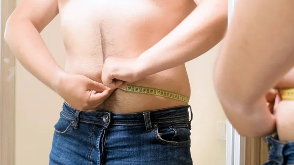 Nahaufnahme eines übergewichtigen Mannes mit Maßband am Spiegel — Stockfoto
