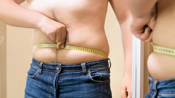 Junger übergewichtiger Mann misst seinen Bauch mit gelbem Klebeband — Stockfoto