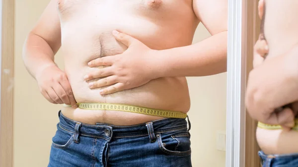 Młody człowiek tłuszczu pomiaru jego duży brzuch w lustro — Zdjęcie stockowe