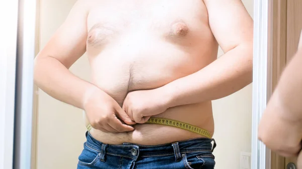 Mladý muž snaží změřit jeho tlusté břicho s nadváhou — Stock fotografie