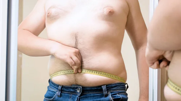 Young man with fat beer belly measuring waist at mirror — Stock Photo, Image