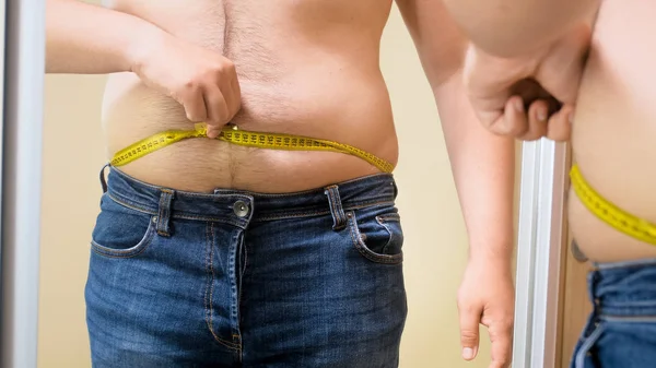 Pemuda gemuk dengan pita pengukur berdiri di cermin — Stok Foto