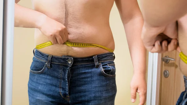Foto de primer plano del hombre con sobrepeso midiendo su gran vientre en el espejo —  Fotos de Stock