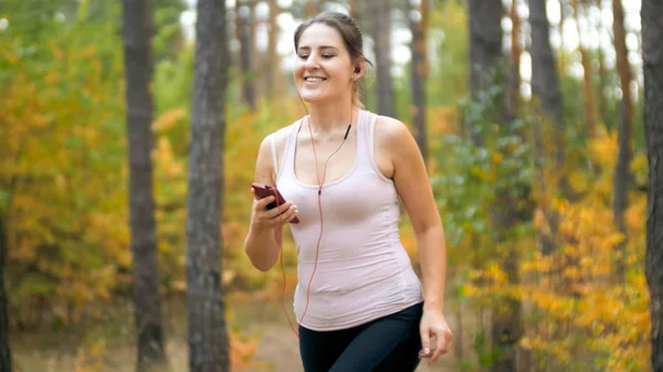 Portrait de femme sportive souriante jooging dans la forêt et écouter de la musique avec des écouteurs — Photo