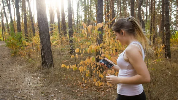 Side view photo of young woman having break while jogging and using smartphone — Stock Photo, Image