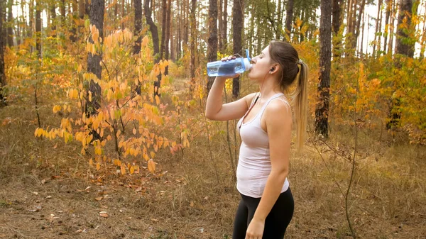Beautiful slim woman srinking water during exercising at forest — Stock Photo, Image