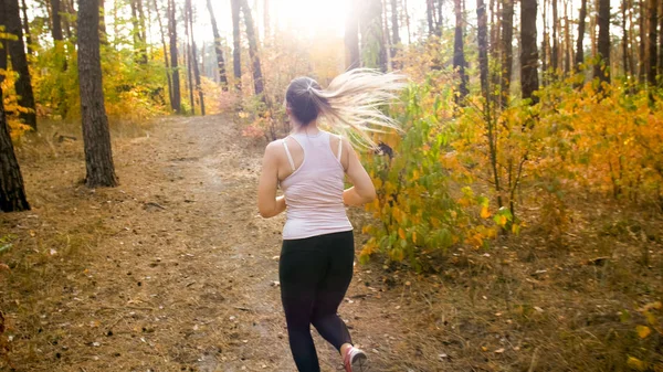 Young slim woman with ponytail jogging in forest at bright sunny day