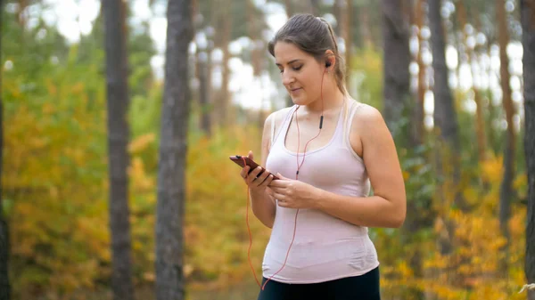 Portrait de jeune femme avec smartphone et écouteurs à la formation en forêt — Photo