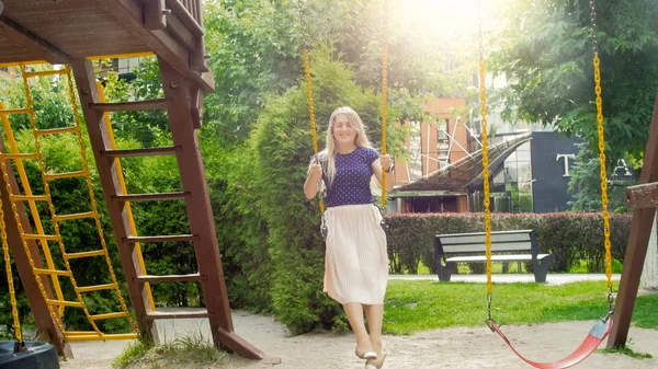 Beautiful blonde woman in long skirt swinging on chain swing at park — Stock Photo, Image