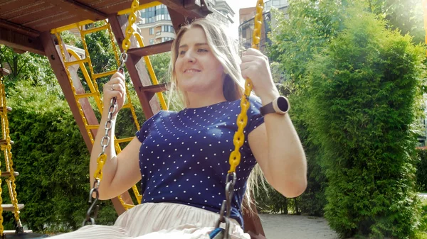 Retrato de una hermosa joven con el pelo largo sentado en el columpio en el patio de recreo — Foto de Stock