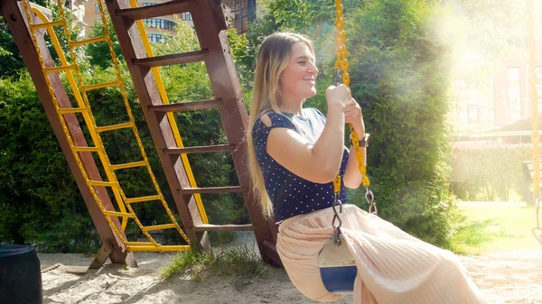 Счастливая улыбающаяся женщина в юбке качается в парке в солнечный летний день — стоковое фото