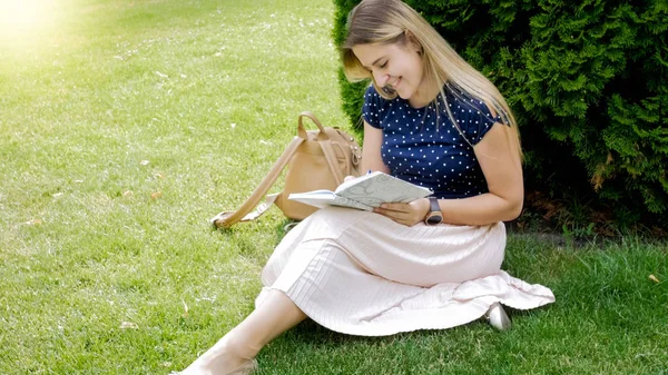 Живая молодая женщина сидит на траве в парке и пишет в блокноте — стоковое фото