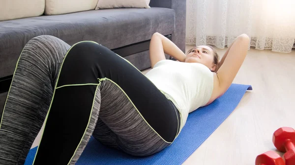 Joven mujer rubia acostada en la colchoneta de fitness en casa y haciendo sentadillas — Foto de Stock