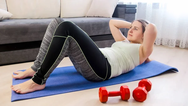 Mujer joven haciendo ejercicios físicos en la alfombra de fitness en casa — Foto de Stock
