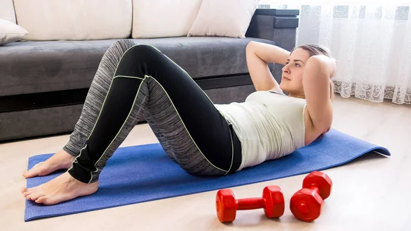 Hermosa joven en leggings haciendo abdominales en el piso en la sala de estar —  Fotos de Stock