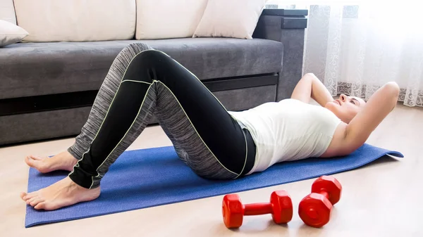 Mujer atlética joven haciendo abdominales en la alfombra de fitness en casa —  Fotos de Stock