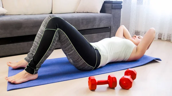 Mujer joven en legging haciendo abdominales crujidos en la alfombra de fitness — Foto de Stock
