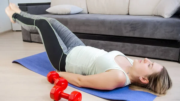 Jonge vrouw liggend op de vloer thuis en doen crunches voor abs en opheffing van de benen — Stockfoto