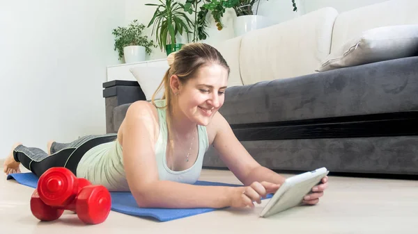 Portrait de femme sportive souriante avec tablette numérique couchée sur florr à la maison — Photo