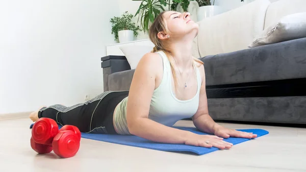 Hermosa mujer joven haciendo ejercicios en la alfombra de fitness en casa — Foto de Stock