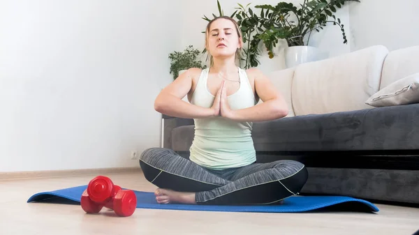 Belle jeune femme assise dans la pose de yoga sur le sol à la maison — Photo