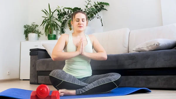 Mujer joven meditando en la esterilla de fitness en la sala de estar —  Fotos de Stock