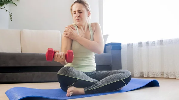 Mujer joven que siente un fuerte dolor en los músculos después de hacer ejercicio con pesas en casa — Foto de Stock