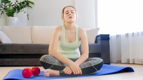 Mujer cansada joven teniendo descanso durante los ejercicios de fitness en la estera en la sala de estar — Foto de Stock