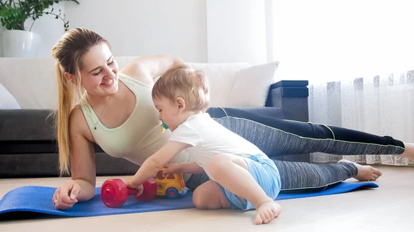 Hermosa madre sonriente haciendo ejercicios de fitness en casa con su niño de 1 año de edad — Foto de Stock