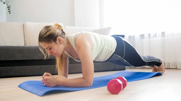 Hermosa mujer joven haciendo ejercicio de tablón en el suelo en la sala de estar — Foto de Stock