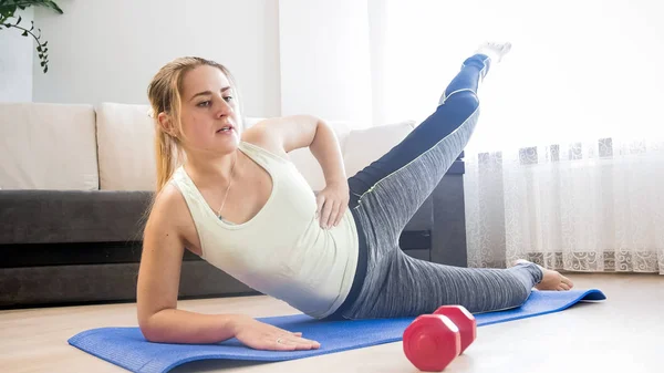 Joven mujer rubia acostada en la alfombra de fitness y levantando la pierna — Foto de Stock