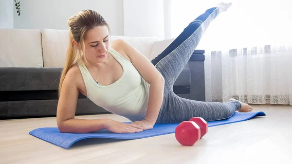 Hermosa mujer joven haciendo ejercicio en el piso levantando la pierna — Foto de Stock