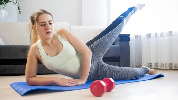 Уставшая молодая женщина делает упражнения на коврике дома — стоковое фото