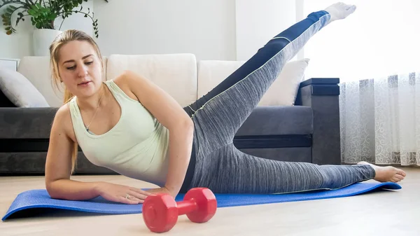 Mujer joven en leggings acostado en la alfombra de fitness y haciendo ejercicios — Foto de Stock